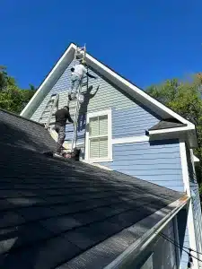 two workers painting a blue house on ladders under a clear sky